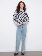 Load image into Gallery viewer, A woman wearing a light blue and dark brown zebra-striped knit sweater with light-wash blue jeans and brown boots standing against a plain white studio background.