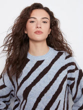 Load image into Gallery viewer, A woman with long, wavy brown hair wearing a light blue knit sweater with bold dark brown zebra-like stripes, photographed against a clean white studio background.