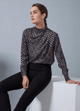 Load image into Gallery viewer, Woman wearing a black and white patterned blouse with black pants against a gray background.