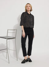 Load image into Gallery viewer, Woman wearing a black and gold patterned blouse and black pants standing next to a chair against a white background.