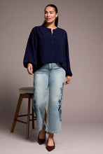 Load image into Gallery viewer, Woman wearing a navy blue top and light blue jeans with floral embroidery and brown heels standing against a plain background.