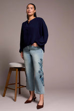 Load image into Gallery viewer, Woman wearing a navy blue top and light blue jeans with floral embroidery and brown heels standing against a plain background.