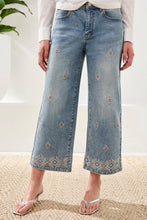 Load image into Gallery viewer, Model wearing light blue jeans with embellishments and sandals standing in a bright room with a plant.