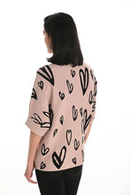 Load image into Gallery viewer, Woman wearing a beige sweater with black heart patterns and rhinestone embellisment and black leggings against a white wall.