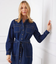 Load image into Gallery viewer, Woman wearing a belted blue denim dress leaning against a white wall.