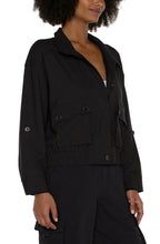 Load image into Gallery viewer, The Brylee utility jacket from Liverpool Los Angeles features a cropped design and cinched hem, perfect for adding a touch of edginess to any outfit. Made with a textured stretch woven fabric, this jacket offers both style and comfort. Stay effortlessly stylish with this versatile piece. Color- Black. Collared. Hidden button placket with zip front closure. Two front flap pockets with double button closure. Button tab at arm to roll sleeves. Cinch waist. Cropped.