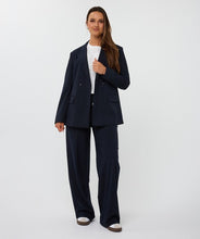 Load image into Gallery viewer, Woman wearing a white top, navy pinstripe blazer and pants and white sneakers against a white background.