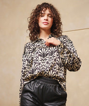 Load image into Gallery viewer, Woman wearing an abstract print top in black and beige and black pants against a beige background.