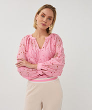 Load image into Gallery viewer, Woman wearing a pink eyelit blouse and tan pants against a grey background.