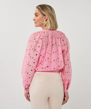 Load image into Gallery viewer, Woman wearing a pink eyelit blouse and tan pants against a grey background.