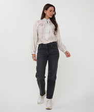 Load image into Gallery viewer, Woman wearing an off-white blouse with a tie detail, dark jeans and white sneakers against a white background.