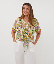 Load image into Gallery viewer, Woman wearing a colorful jungle patterned short sleeve blouse and white pant against a white background.