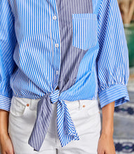 Load image into Gallery viewer, Close-up of a person wearing a blue, grey and white striped shirt with a tied front, standing on a blurred outdoor background.