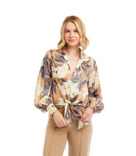 Load image into Gallery viewer, Woman wearing a tie waist patterned long sleeve blouse in floral grey, cream and tan and tan pants against a neutral background.