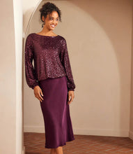 Load image into Gallery viewer, Woman wearing a purple sequin long sleeve blouse and purple silk skirt standing against a beige wall.