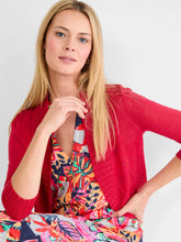 Load image into Gallery viewer, Woman wearing a red bolero cardigan over a colorful floral dress against a white background.