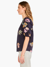 Load image into Gallery viewer, Sometimes it's all in the name! This dramatic combo of dark background and powerful pops of color on this stunning top is an outfit scene stealer, a real conversation piece. It's not just the firework display design though: we love the layered details on the short sleeves, the easy elastic cuffs, the frilled split neck, and the tie front. Dress it up with professional workpants or keep things casual with denim.