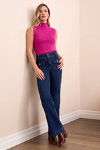 Load image into Gallery viewer, Woman wearing a pink sleeveless top, blue jeans and brown boots standing against a beige wall.
