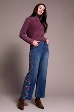 Load image into Gallery viewer, Woman sitting on a stool wearing a purple sweater, blue jeans with floral embroidery and black boots against a neutral background.