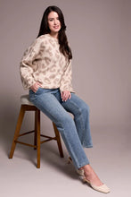 Load image into Gallery viewer, Woman sitting on a stool wearing a sequined beige chetah print sweater, blue jeans with tiny rhinestones and beige heels against a plain background.