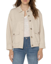 Load image into Gallery viewer, Woman wearing a tan button front jacket over a white tee and blue jeans against a white background.