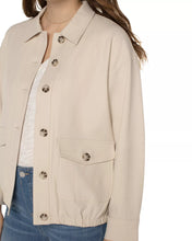 Load image into Gallery viewer, Woman wearing a tan button front jacket over a white tee and blue jeans against a white background.