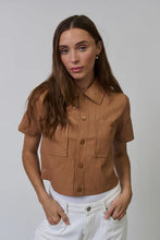 Load image into Gallery viewer, Woman wearing a brown short-sleeve faux leather shirt and white pants with a plain background.