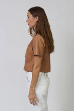Load image into Gallery viewer, Woman wearing a brown faux leather short sleeve top and white pants against a plain background.