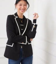 Load image into Gallery viewer, Woman wearing a black blazer with cream trim over a black and white stripe top and blue jeans against a white wall.