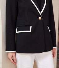 Load image into Gallery viewer, Close-up of black blazer with cream trim and cream pants against a beige background.