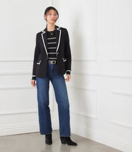 Load image into Gallery viewer, Woman wearing a black blazer with cream trim over a black and white stripe top, blue jeans and black boots against a white wall.