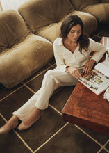 Load image into Gallery viewer, Woman sitting on the floor, next to a couch, reading a magazine and wearing a corduroy cream top, matching pants and beige flats.