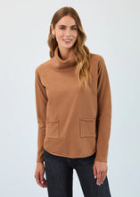 Load image into Gallery viewer, Woman wearing a bronze caramel cowl neck sweater with front pockets, small hoop earrings and dark wash jeans against a light gray background.