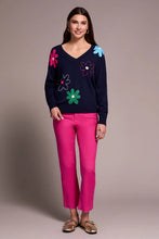Load image into Gallery viewer, Woman wearing a navy sweater with colorful flower patterns, bright pink pants and metallic flats against a neutral background.