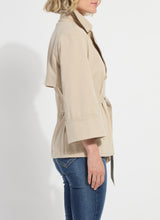Load image into Gallery viewer, Woman wearing a beige trench and blue jeans against a white background.