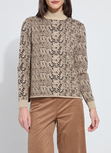 Load image into Gallery viewer, Model wearing a lux camel colored snake jacquard patterned sweater and brown pants against a white background.