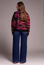 Load image into Gallery viewer, Woman wearing a colorful patterned cardigan, blue jeans and heeled boots against a plain background.