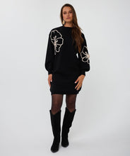 Load image into Gallery viewer, Woman wearing a black dress with floral designs and black knee-high boots against a white background.