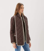 Load image into Gallery viewer, A woman modeling a dark brown diamond-quilted jacket with cream-colored trim along the edges styled with a brown ribbed top and blue jeans against a plain light gray background.