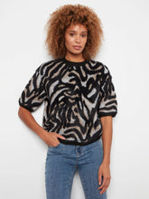 Load image into Gallery viewer, A woman with curly brown hair wearing a black and beige zebra-print knit sweater and blue jeans, standing against a plain white background.
