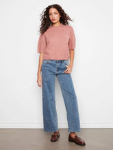 Load image into Gallery viewer, A woman stands against a white wall wearing a dusty pink short-sleeve knit top, wide-leg blue jeans, and brown leather loafers.