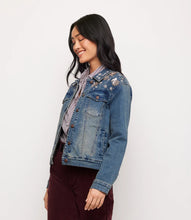 Load image into Gallery viewer, A woman wearing a blue denim jacket with floral embroidery and rhinestones on the shoulders, layered over a striped shirt and dark burgundy pants, photographed against a plain white studio background.