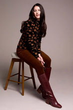 Load image into Gallery viewer, Woman sitting on a stool wearing a black velvet with tonal flowers top, brown pants with burgundy boots against a plain background.