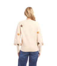 Load image into Gallery viewer, Woman wearing a cream sweater with embroidered flowers and blue jeans against a white background.
