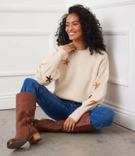 Load image into Gallery viewer, Woman sitting on the floor wearing a cream floral embroidered sweater, blue jeans, and brown knee-high boots.