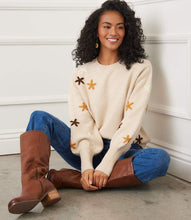 Load image into Gallery viewer, Woman sitting on the floor wearing a cream floral embroidered sweater, blue jeans, and brown knee-high boots.