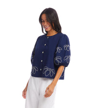 Load image into Gallery viewer, The Emely Embroidered Puff Sleeve Shirt by Karen Kane is a perfect blend of structured elegance and feminine charm. Featuring intricate white embroidery on a navy blue background, this stylish top adds a refined touch to any outfit. The puff sleeves create a statement look, while the pleated back detail enhances its flattering silhouette.