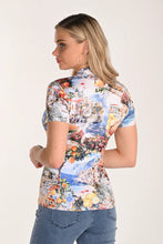 Load image into Gallery viewer, Woman wearing a colorful short-sleeve shirt with a scenic print and blue jeans on a plain background.