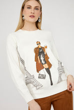 Load image into Gallery viewer, Woman wearing a sweater with a graphic design of a woman in a coat and Eiffel Tower and brown pants against a white background.
