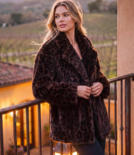 Load image into Gallery viewer, A woman wearing a dark brown leopard-print faux fur coat stands on a balcony at sunset with a vineyard in the background.